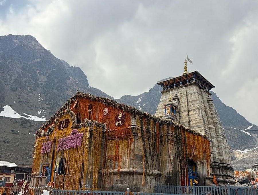 Kedarnath Temple, hung with marigold garlands, below cloud and rocky, snow-patched mountains.